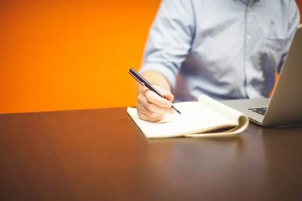 A person writing notes beside a laptop