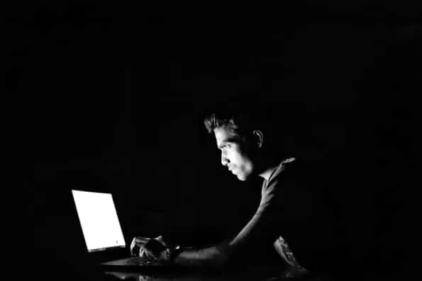A person lit only by a laptop screen in a dark room