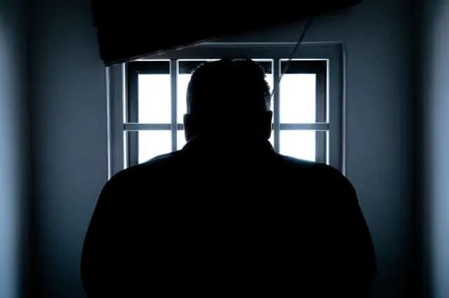 A silhouetted figure at a barred prison window