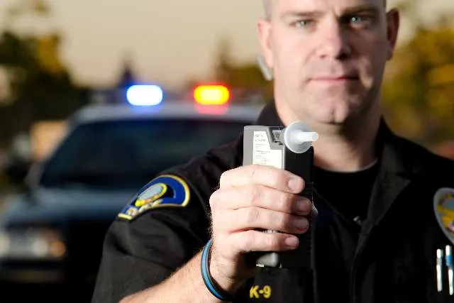 A police officer holding a breathalyzer beside a patrol car
