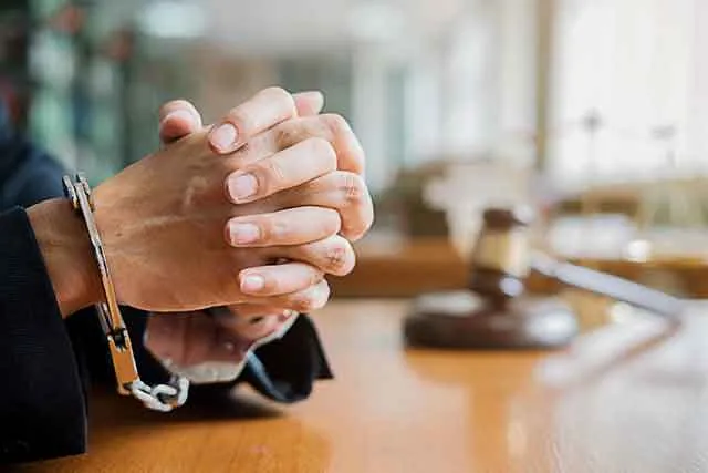 Handcuffed hands resting on a table beside a gavel