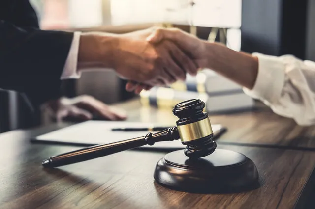 A handshake over a desk with a gavel in the foreground