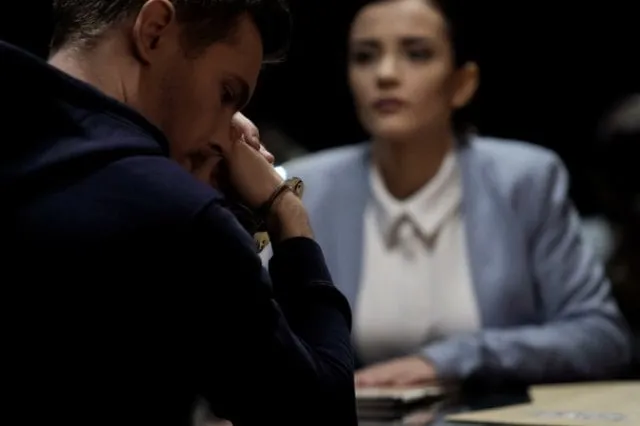 A worried man and a woman seated at a table during questioning