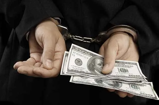 Handcuffed hands holding hundred-dollar bills