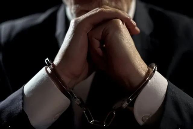 A person in a suit with handcuffed hands
