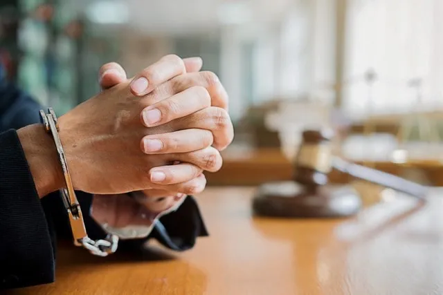 Handcuffed hands on a table with a gavel behind them