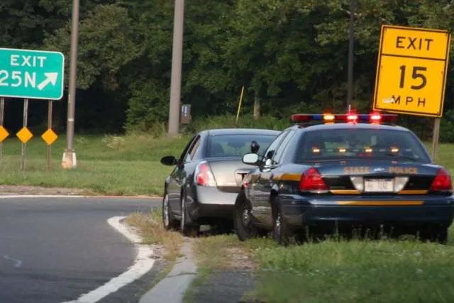 A police car stopped behind a vehicle on a highway exit ramp