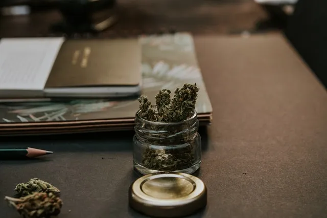 A jar of cannabis on a desk beside a notebook