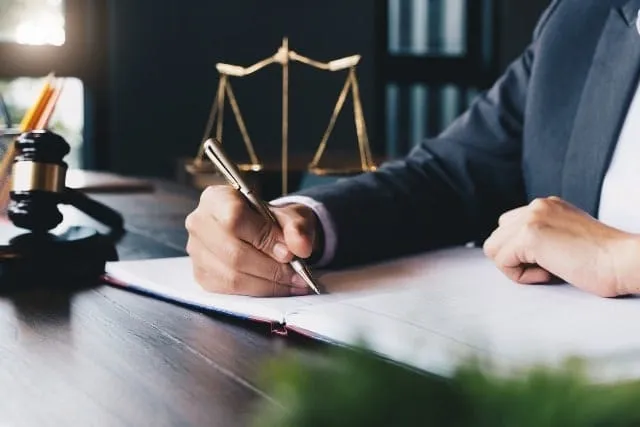 Scales of justice and a gavel on a desk beside a person writing