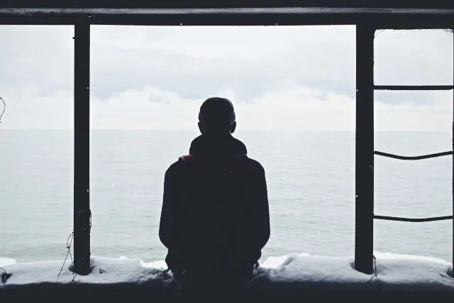 A person sitting alone on a pier looking out to sea