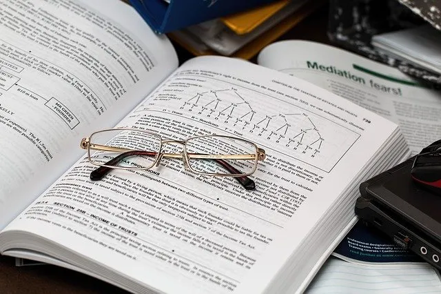 An open reference book with reading glasses resting on it