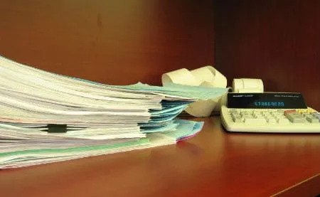 Paperwork spilling across a desk beside an adding machine