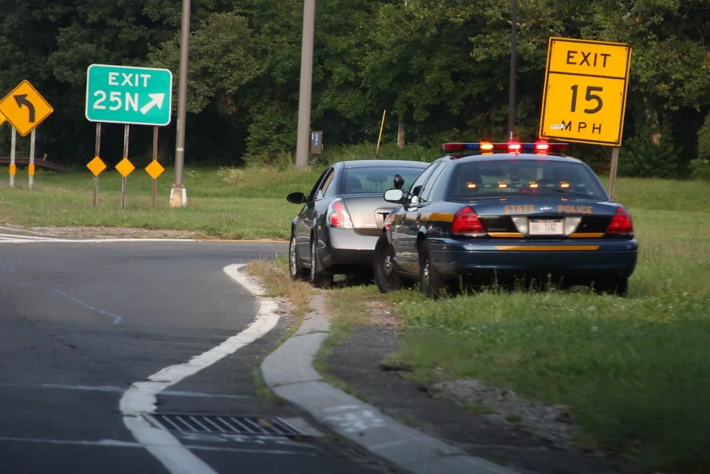 A police car stopped behind a vehicle on a highway exit ramp