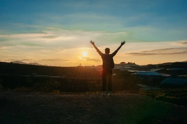 A person standing with arms raised at sunrise