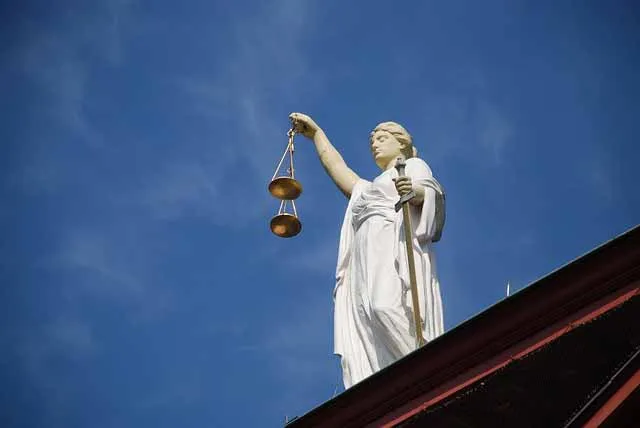 A statue of Lady Justice with scales, seen against the sky