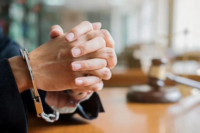 Handcuffed hands on a courtroom table beside a gavel