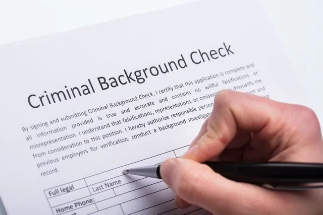 A hand completing a criminal background check form